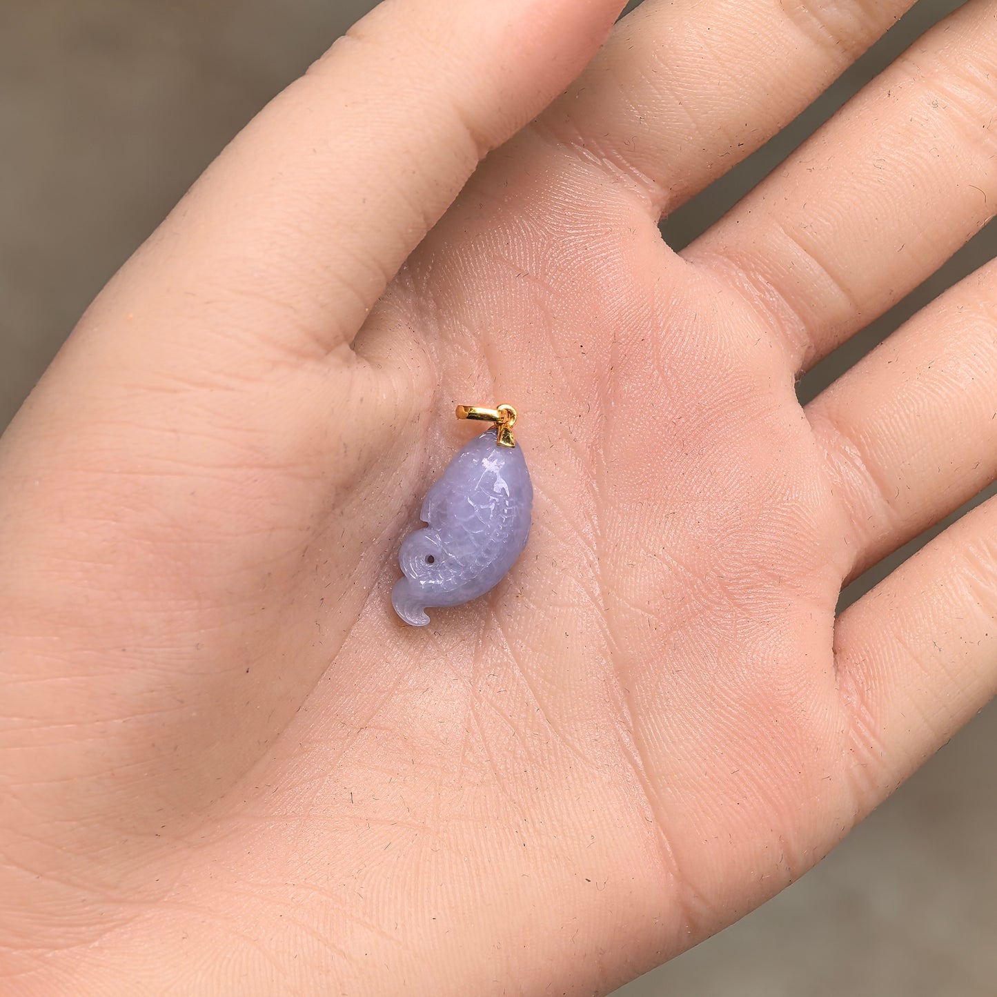 Natural Grade-A glutinous lavender fish jadeite pendant with 18K gold bail shown in hand.
