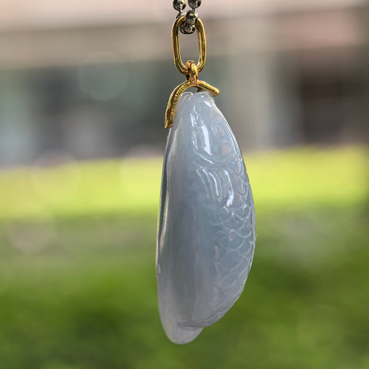 Side view of rich lavender fish jadeite pendant showing three-dimensional carved body.
