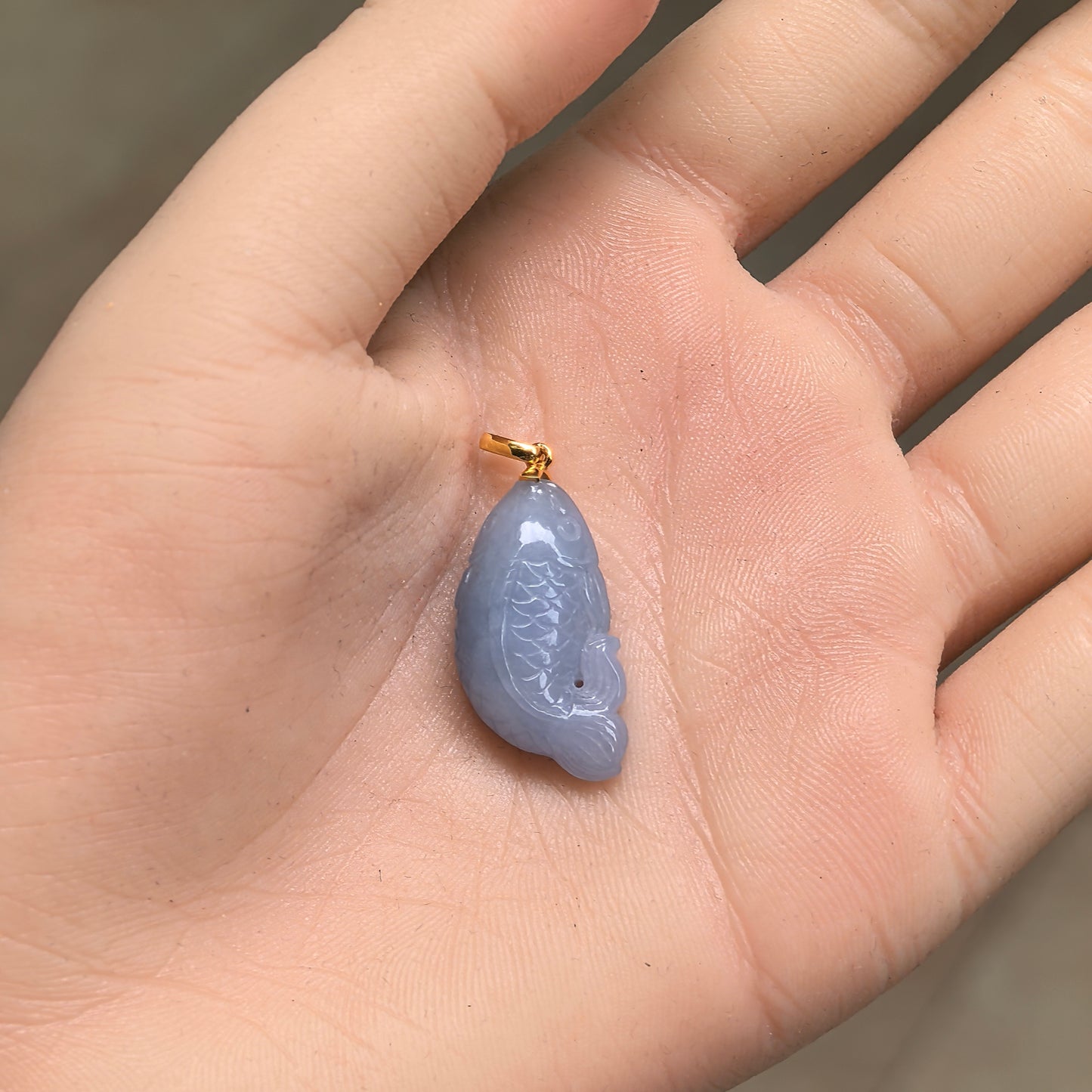 Glutinous lavender jadeite fish pendant shown in hand with gold bail and compact size.
