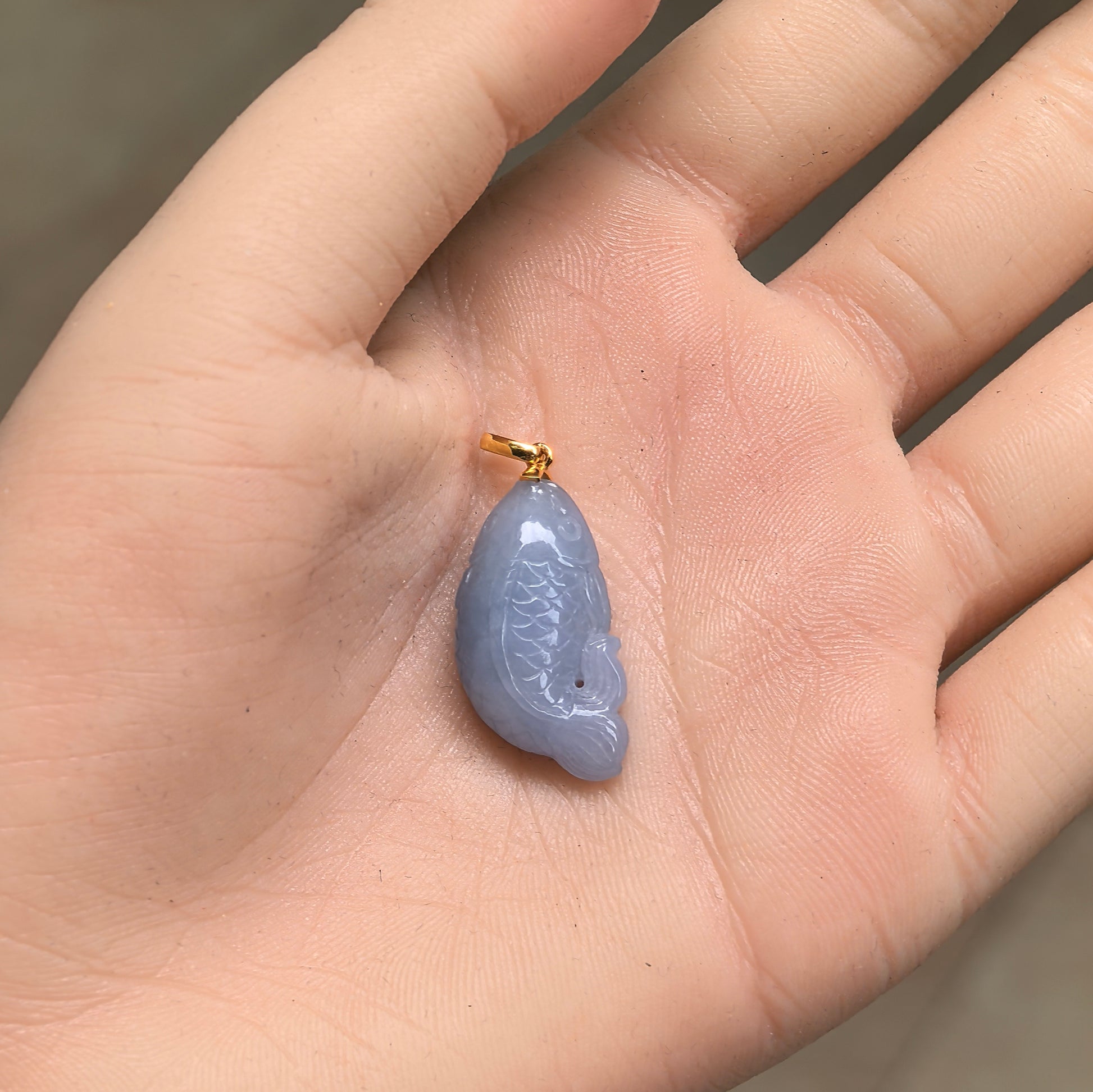 Glutinous lavender jadeite fish pendant shown in hand with gold bail and compact size.
