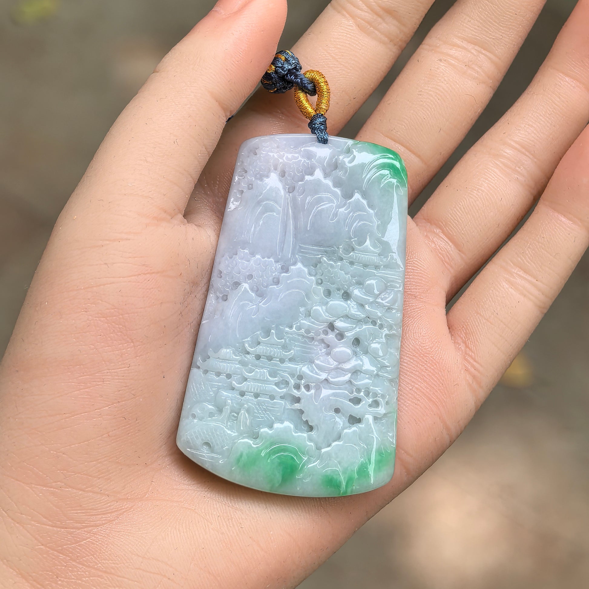 Large white-base green jadeite landscape pendant shown in hand with detailed mountain and pavilion carving.
