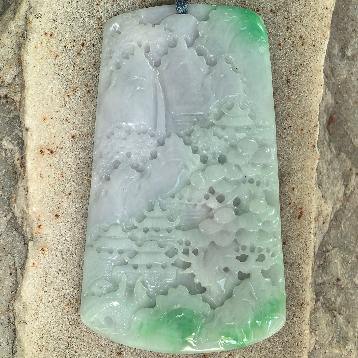 Close-up of glutinous white-base green jadeite landscape plaque showing carved scenery and soft luster.

