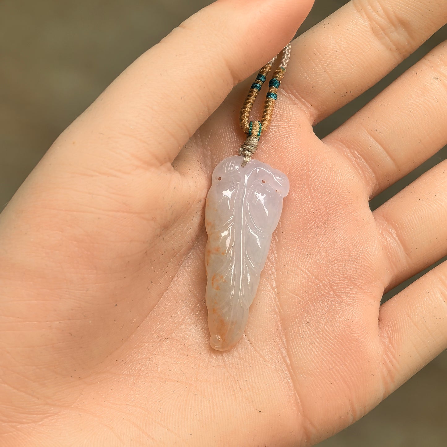White-base golden-splash jadeite leaf pendant shown in hand with carved vein details.
