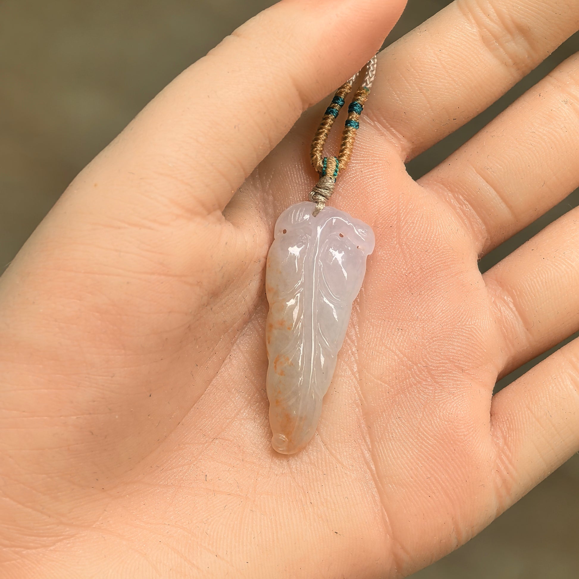 White-base golden-splash jadeite leaf pendant shown in hand with carved vein details.
