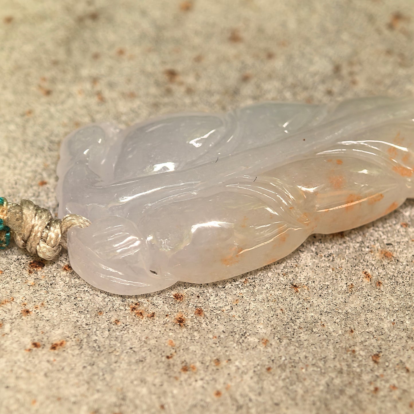 Close-up of natural jadeite leaf pendant showing polished surface and warm golden-brown splashes.
