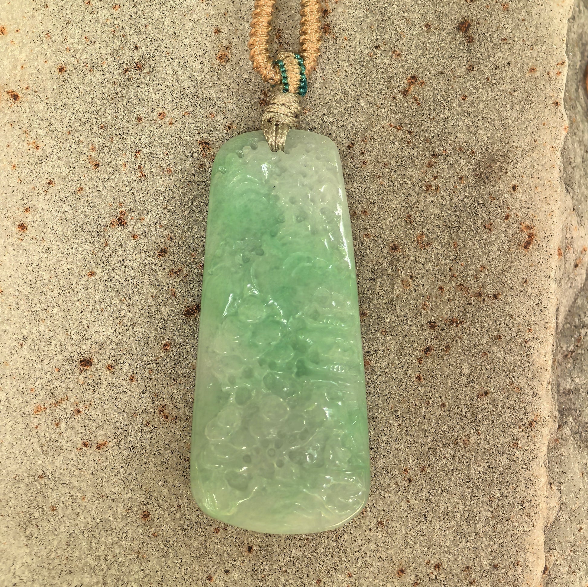 Close-up of glutinous white-base green jadeite pendant showing carved mountain and pavilion scenery.
