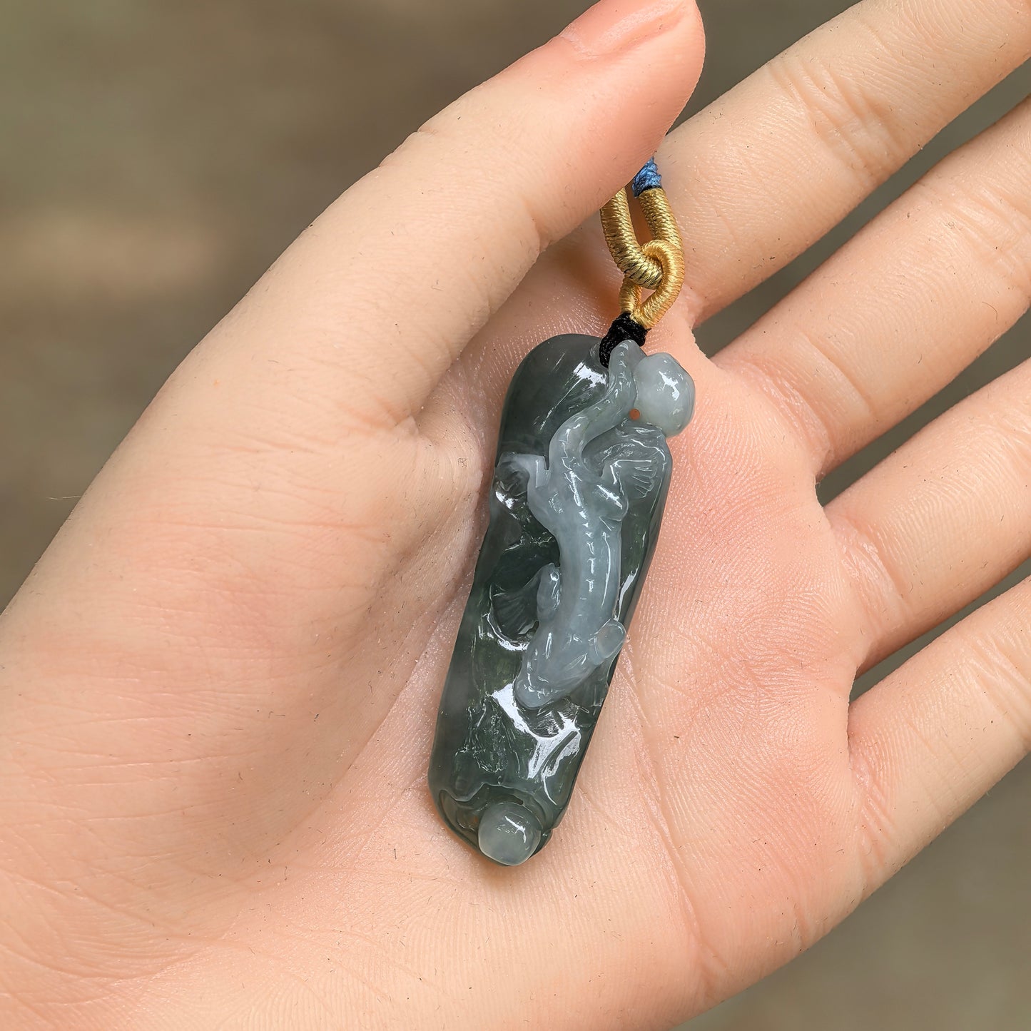 Oil green chi-dragon jadeite pendant shown in hand with three-dimensional carved details.
