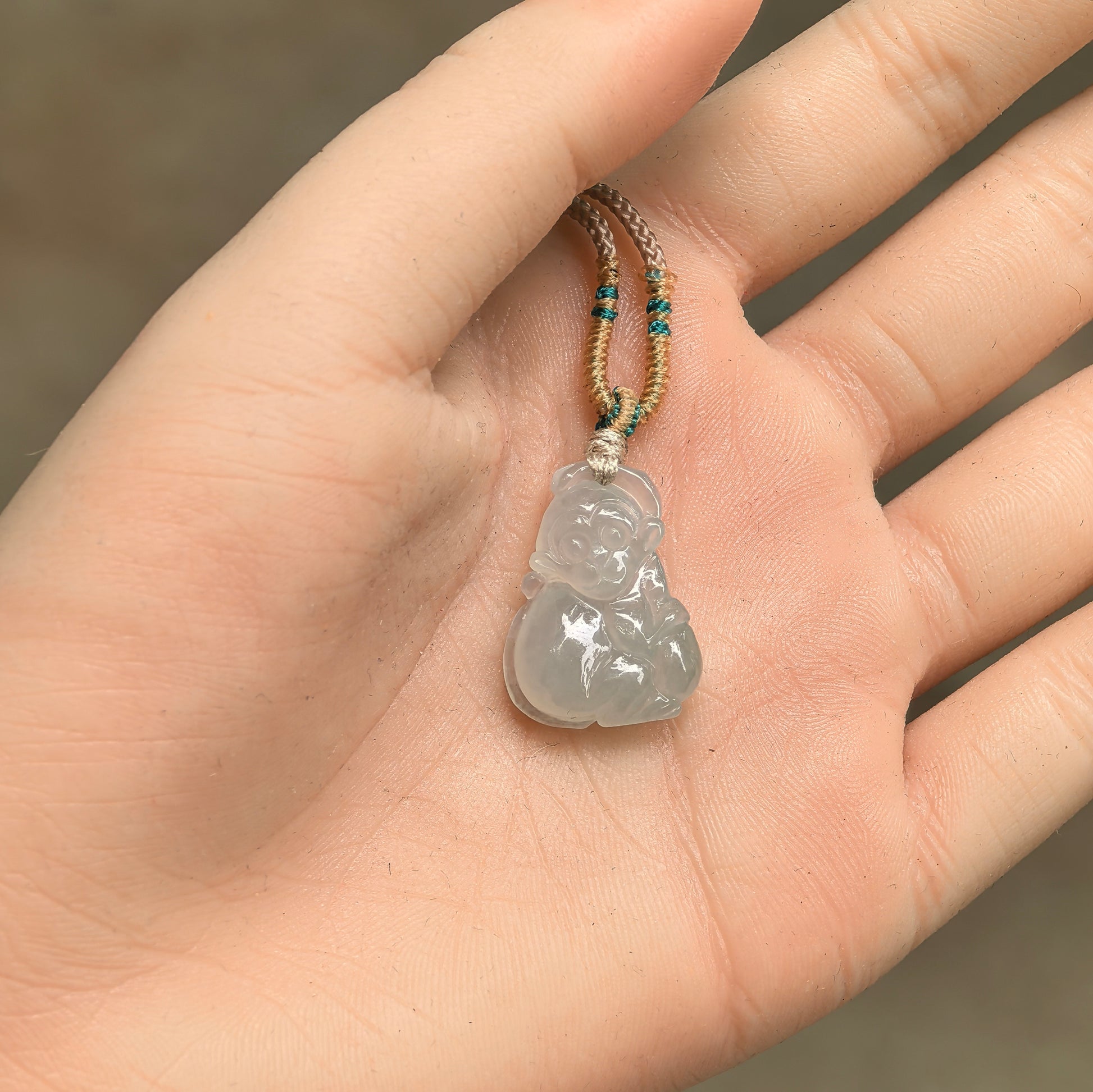 Light green base monkey jadeite pendant shown in hand with petite three-dimensional carving.
