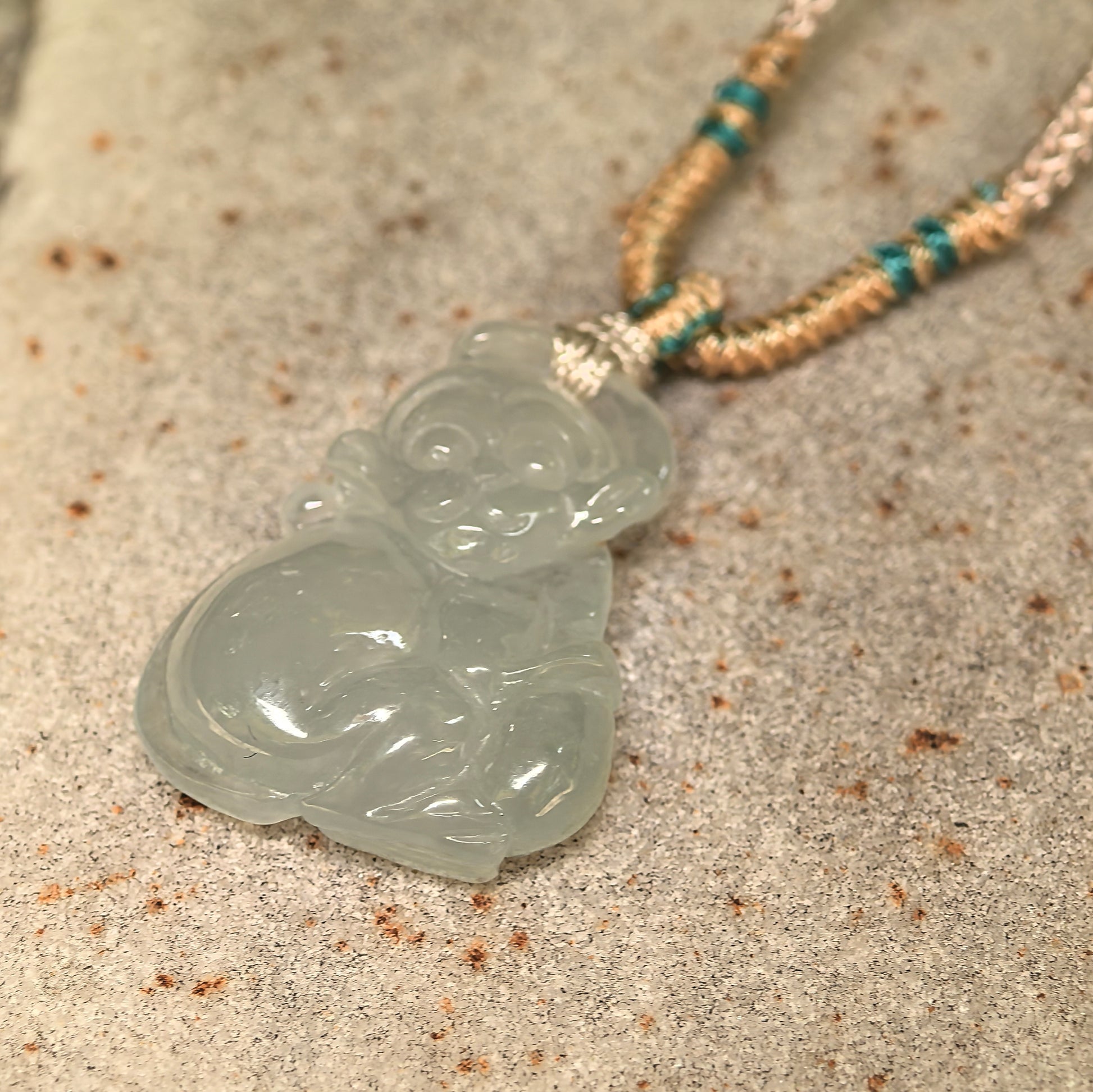 Close-up of icy glutinous monkey jadeite pendant showing smooth carved details and glossy surface.
