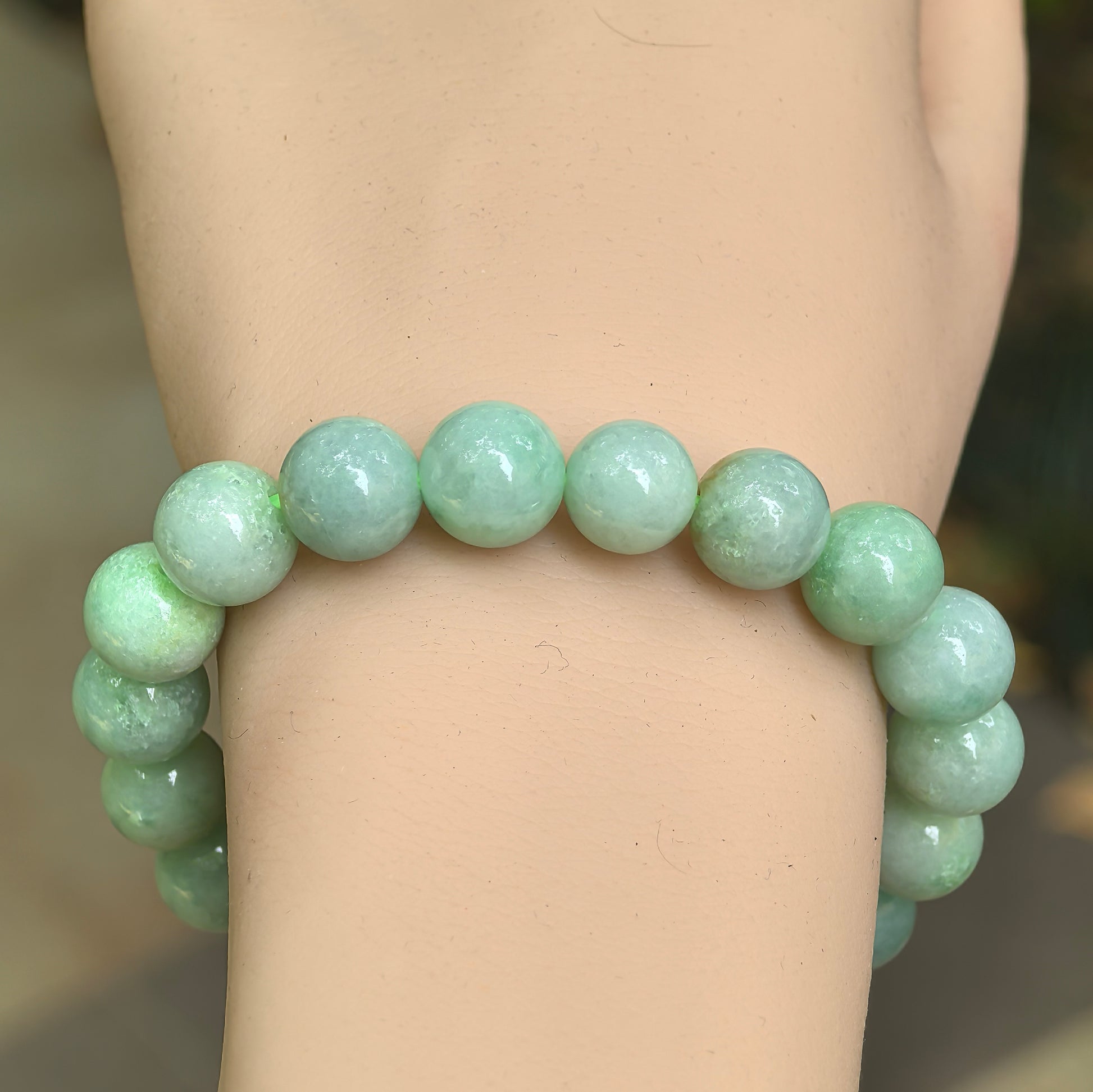 Close-up of apple green jadeite bracelet on wrist with natural cloudy texture and glossy round beads.
