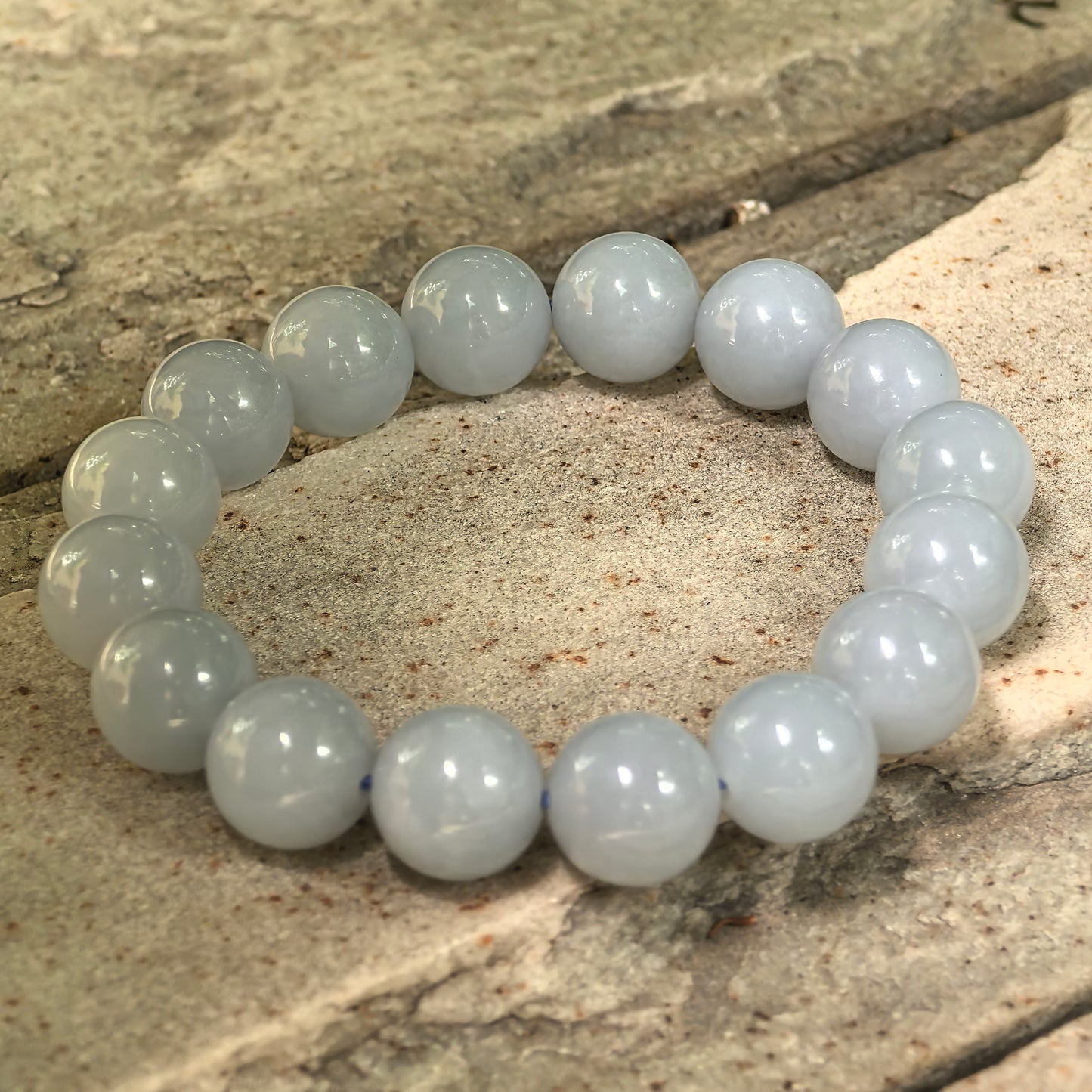 Natural Grade-A blue-lavender jadeite bead bracelet shown on stone background with glossy finish.
