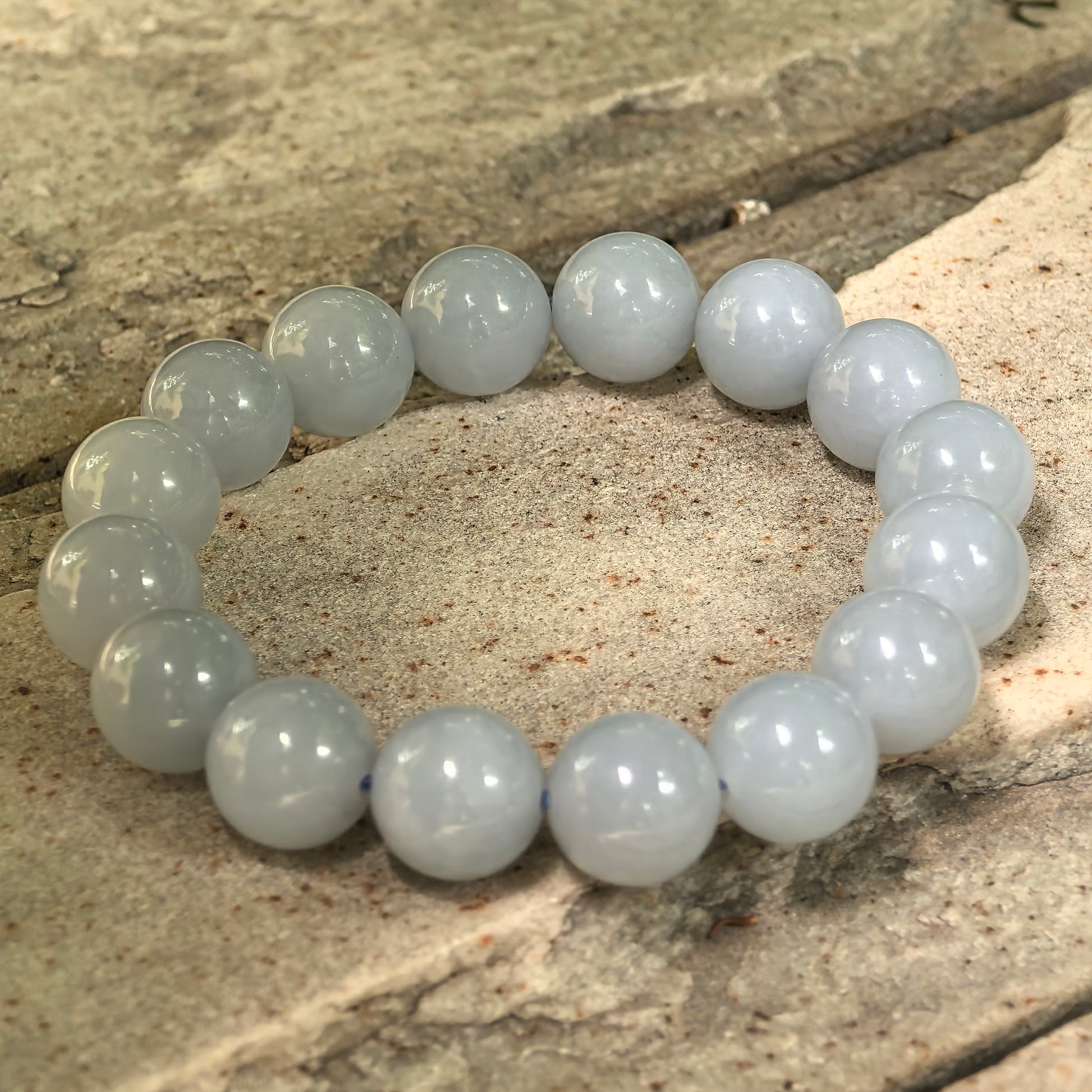 Natural Grade-A blue-lavender jadeite bead bracelet shown on stone background with glossy finish.
