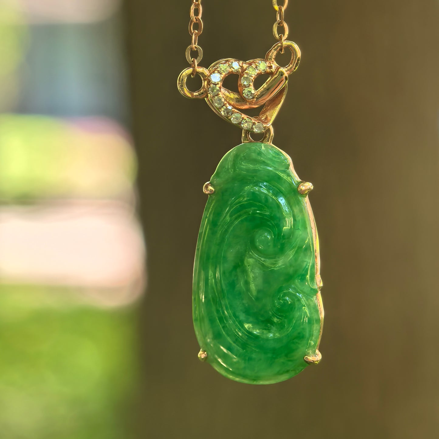 Natural Grade-A glutinous green Ruyi jadeite pendant in 18K gold hanging on a gold chain.
