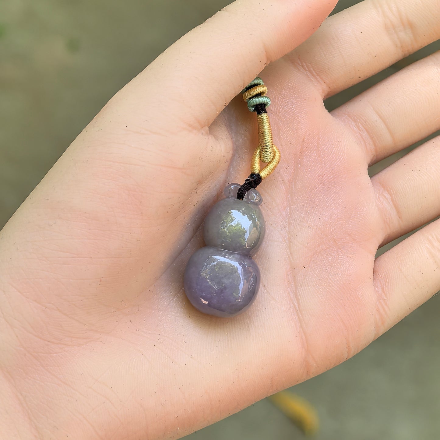 Natural Grade-A glutinous lavender and light green gourd jadeite pendant shown on hand with cord.
