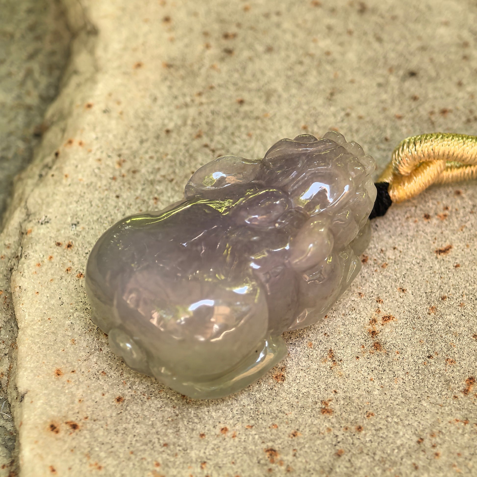 Natural Grade-A lavender purple Pixiu jadeite pendant displayed on stone with soft luster.
