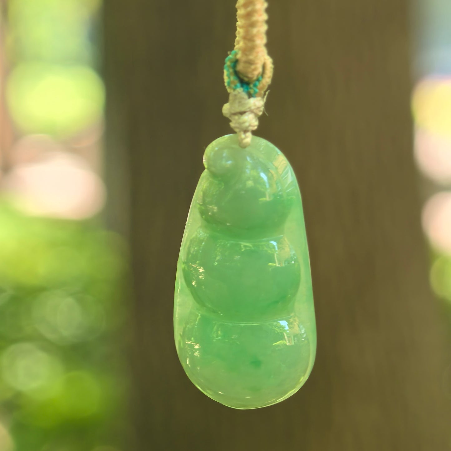 Natural Grade-A glutinous green bean jadeite pendant hanging on cord with soft green translucency.
