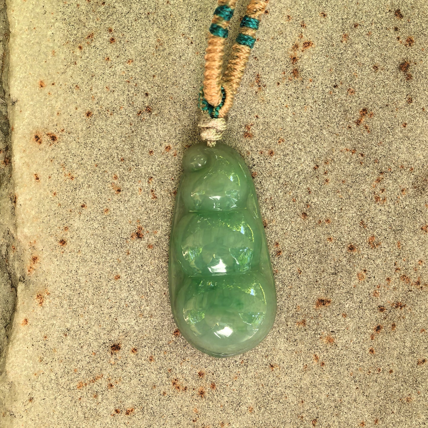Close-up of glutinous green bean jadeite pendant on stone surface with natural cloudy texture.
