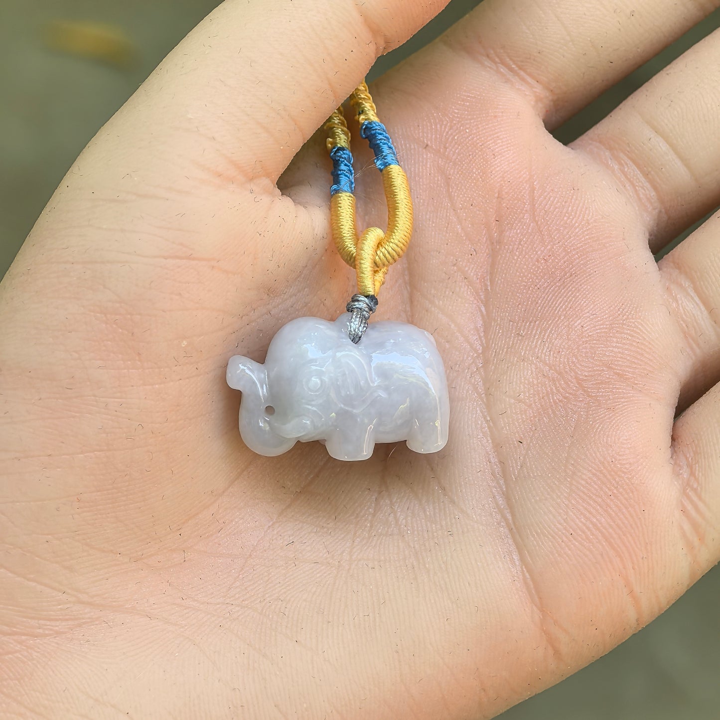 White three-dimensional elephant jadeite pendant displayed in hand with compact rounded carving.

