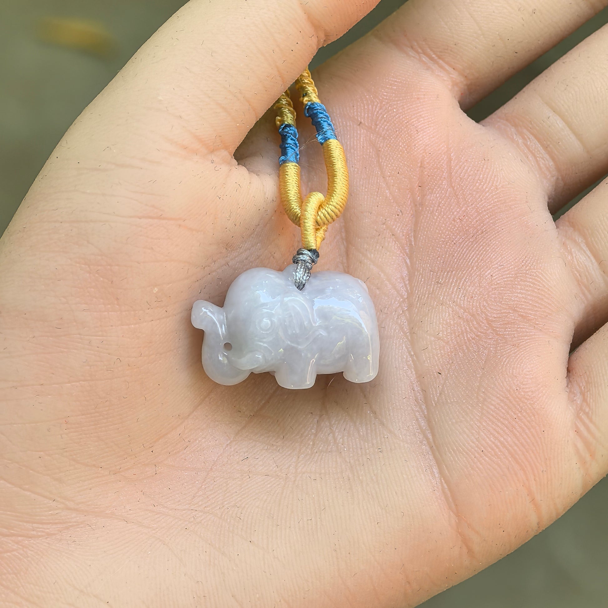 White three-dimensional elephant jadeite pendant displayed in hand with compact rounded carving.
