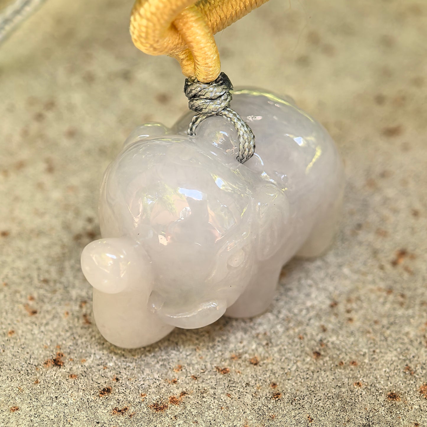 Natural Grade-A white elephant jadeite pendant on stone surface with cord detail.
