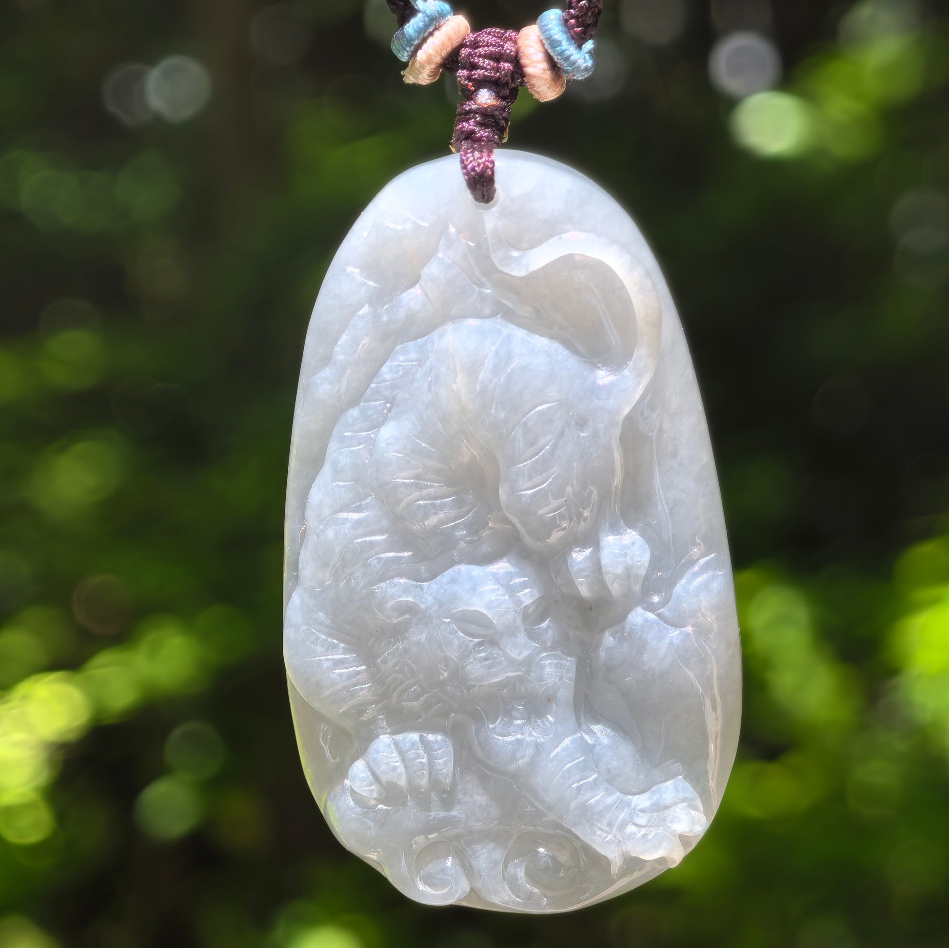 Natural Grade-A glutinous pale green tiger jadeite pendant hanging on cord against a green background.
