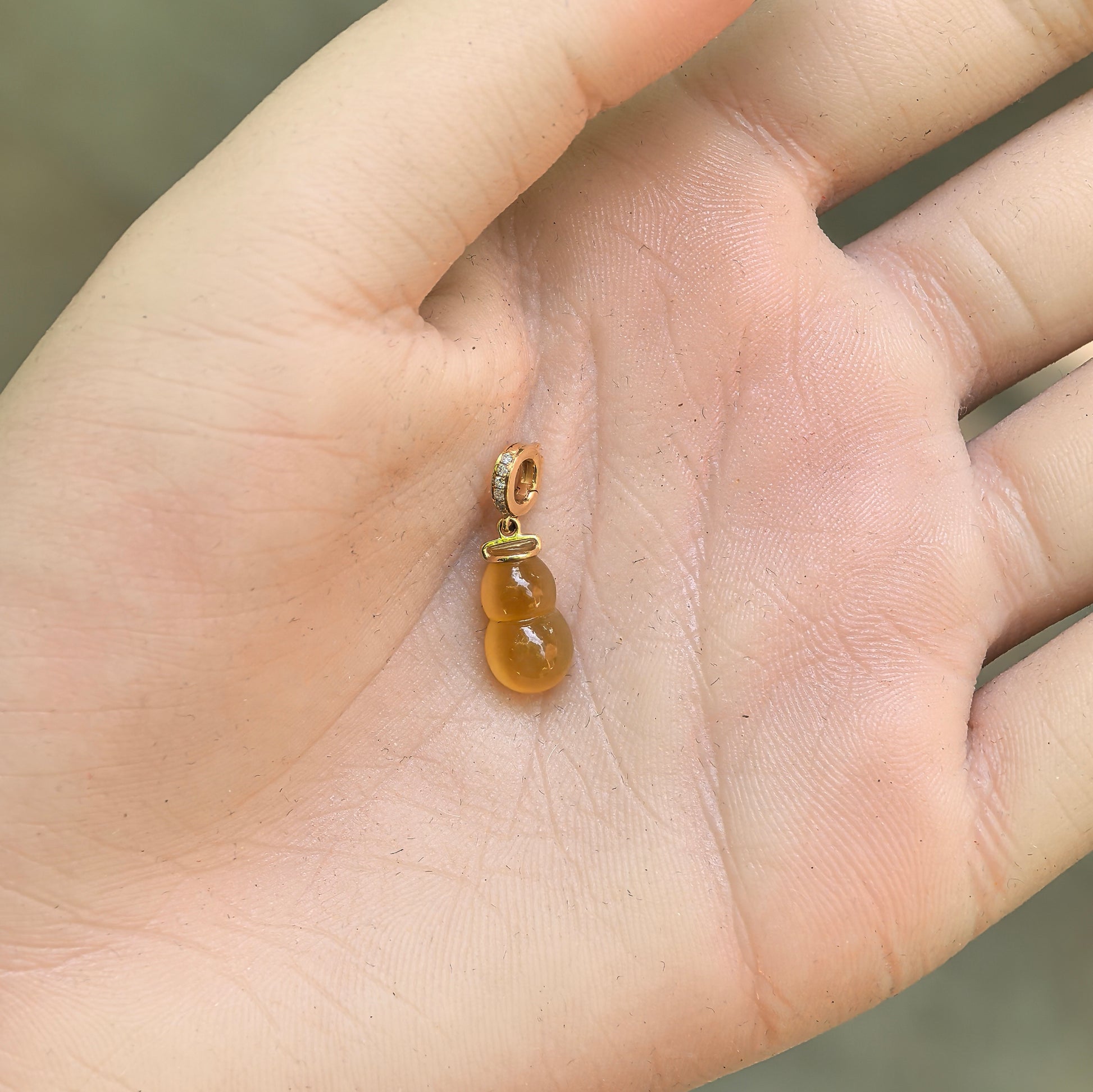 Small yellow gourd jadeite pendant shown on hand with 18K gold setting and diamond accents.
