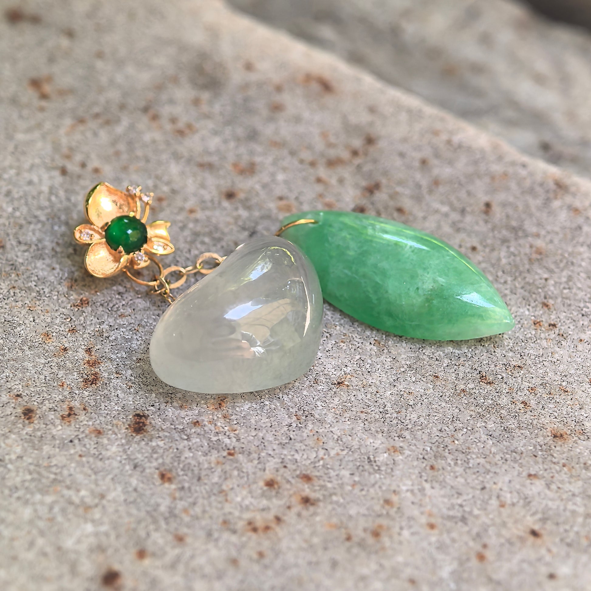 Natural Grade-A white heart and green drop jadeite pendant displayed on stone surface with 18K gold detail.