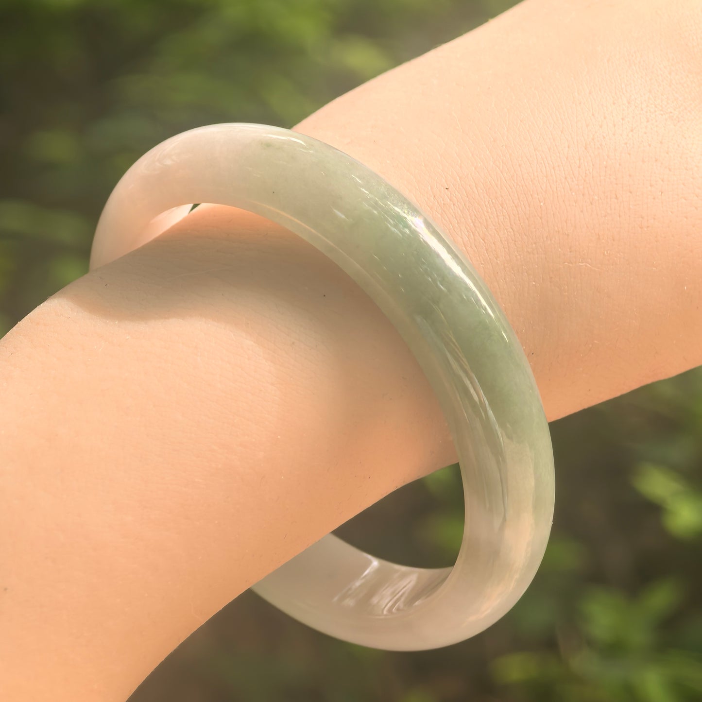 Natural Grade-A glutinous white and deep green D-shape jadeite bangle worn on wrist in natural light.
