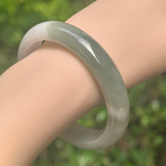 Natural Grade-A glutinous white green D-shape jadeite bangle displayed on wrist with classic rounded profile.
