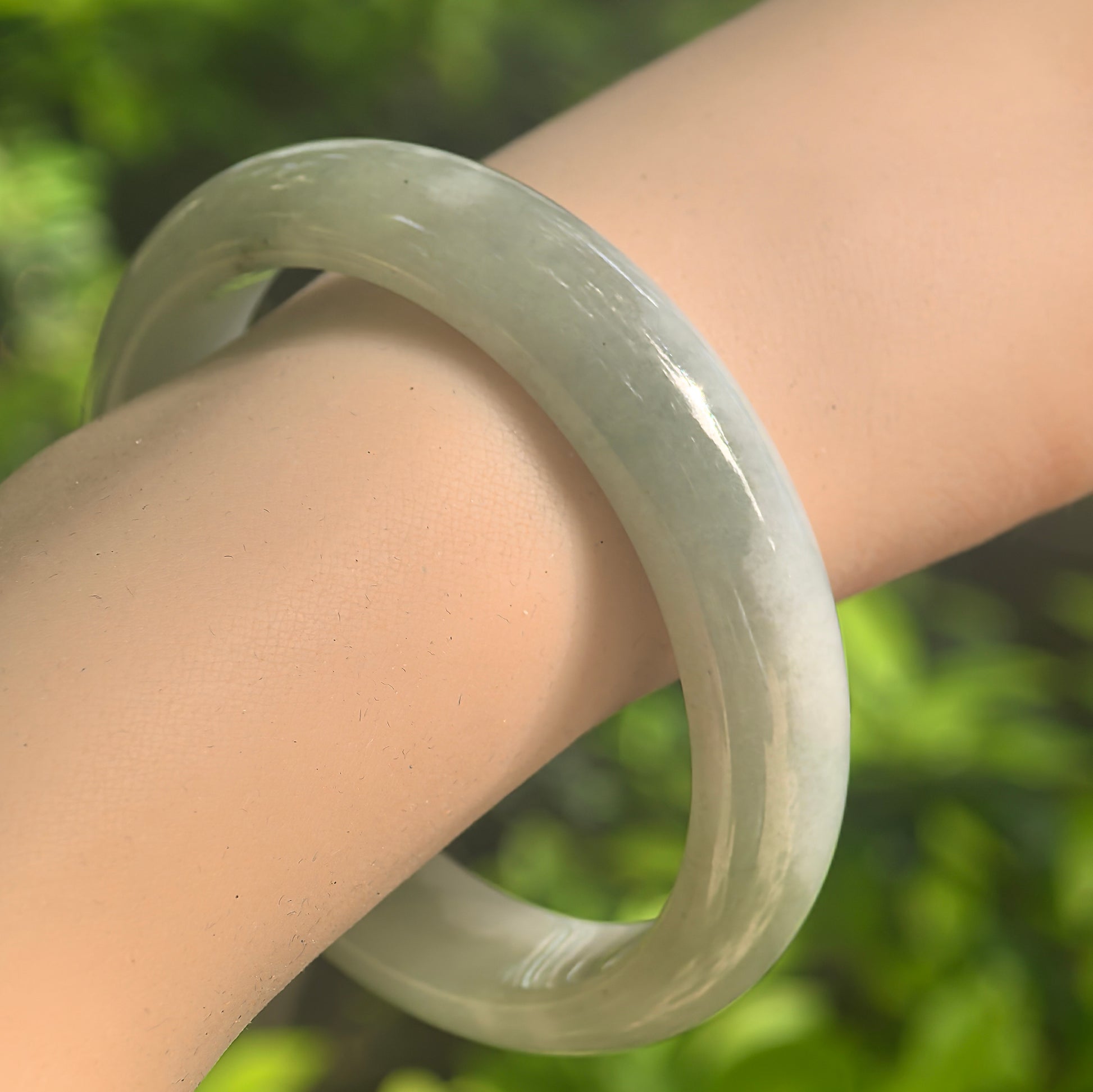 Natural Grade-A fine glutinous light green D-shape jadeite bangle worn on wrist in natural light.
