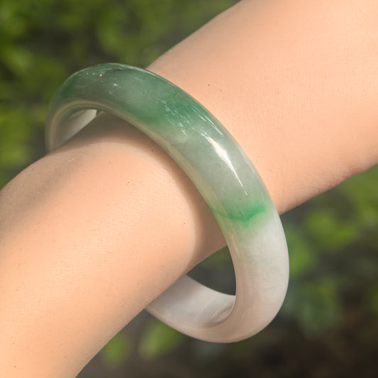 Natural Grade-A fine glutinous white-base green D-shape jadeite bangle worn on wrist in natural light.