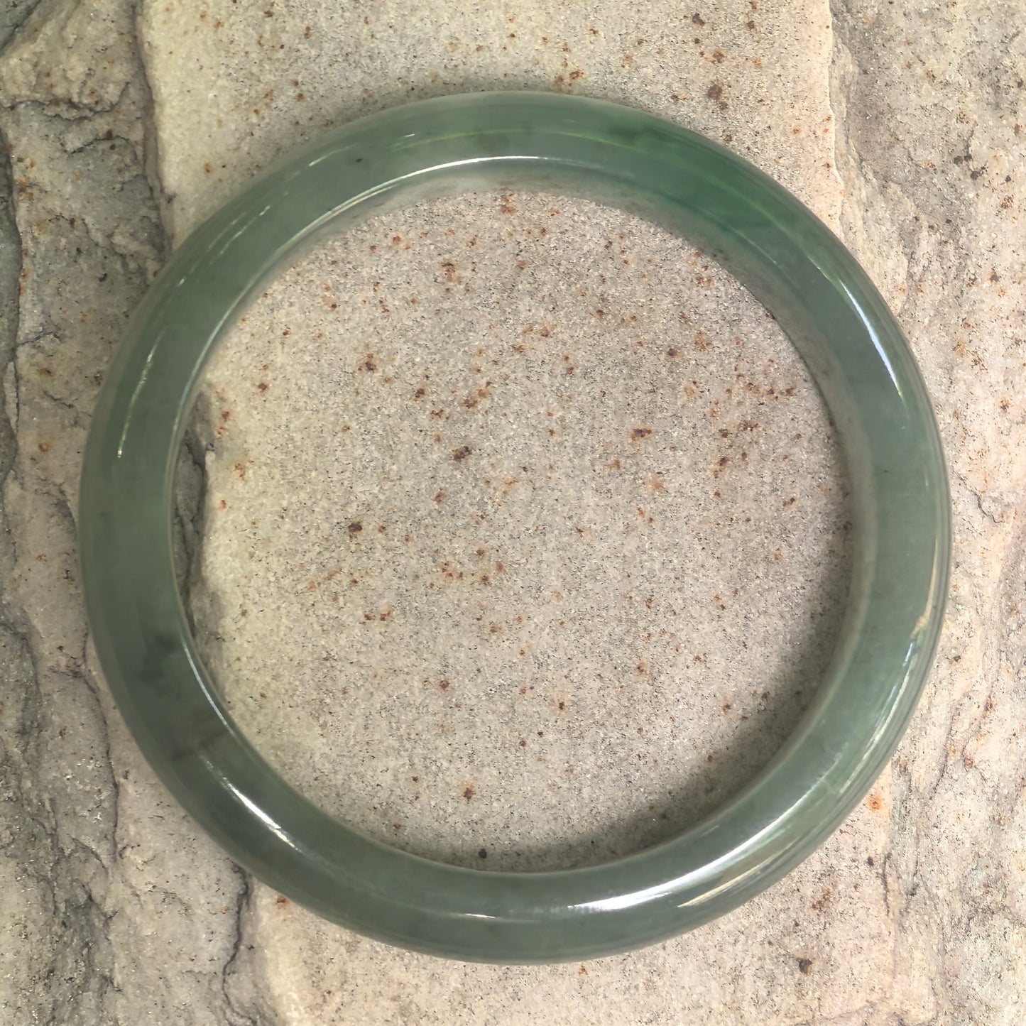 Close-up of oil green jadeite bangle showing smooth polish and cottony inclusions.
