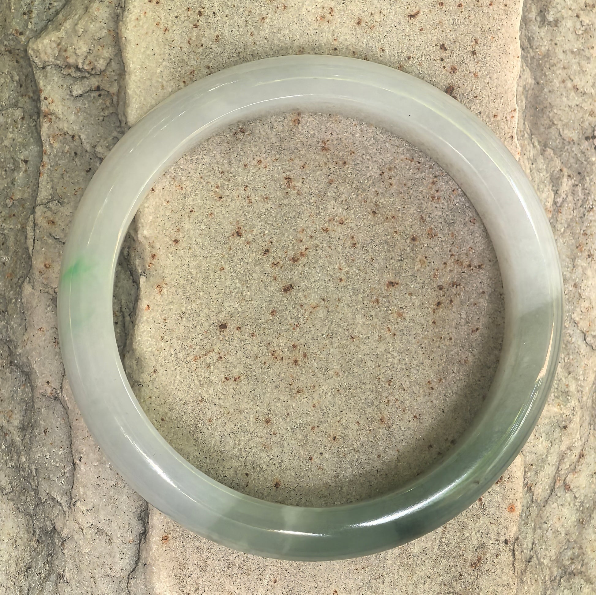 Close-up of white base dark green jadeite bangle showing polished surface and natural black specks.
