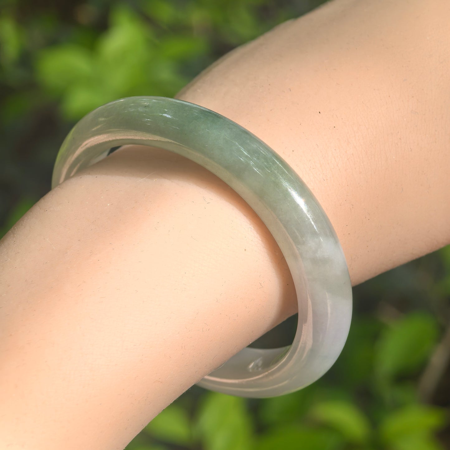 Natural Grade-A glutinous white and dark green oval jadeite bangle worn on the wrist in natural light.
