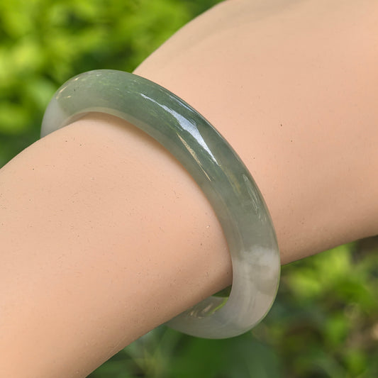 Close-up of an oval white and dark green jadeite bangle showing smooth polish and natural color contrast.
