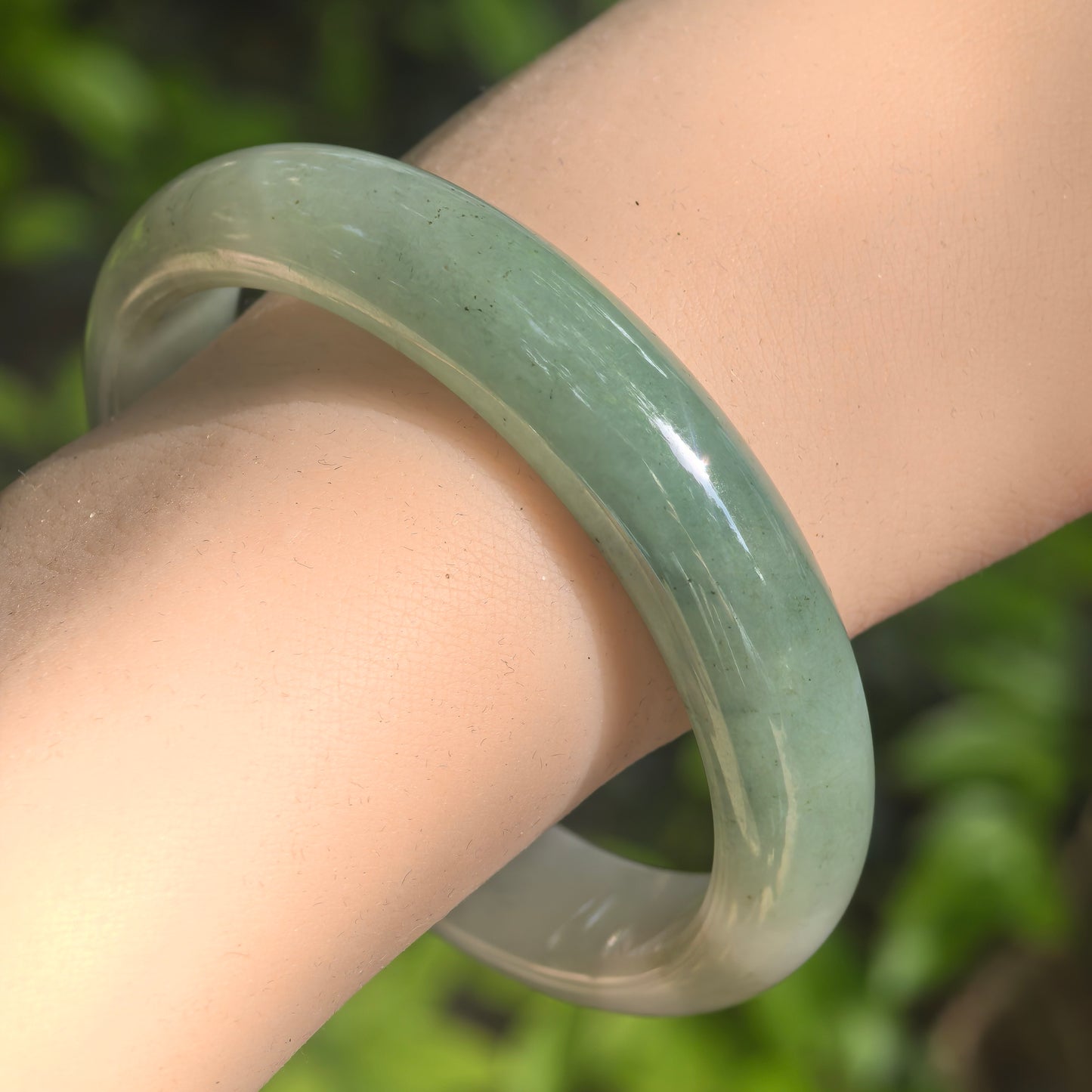 Natural Grade-A glutinous light green D-shape jadeite bangle worn on the wrist in natural light.
