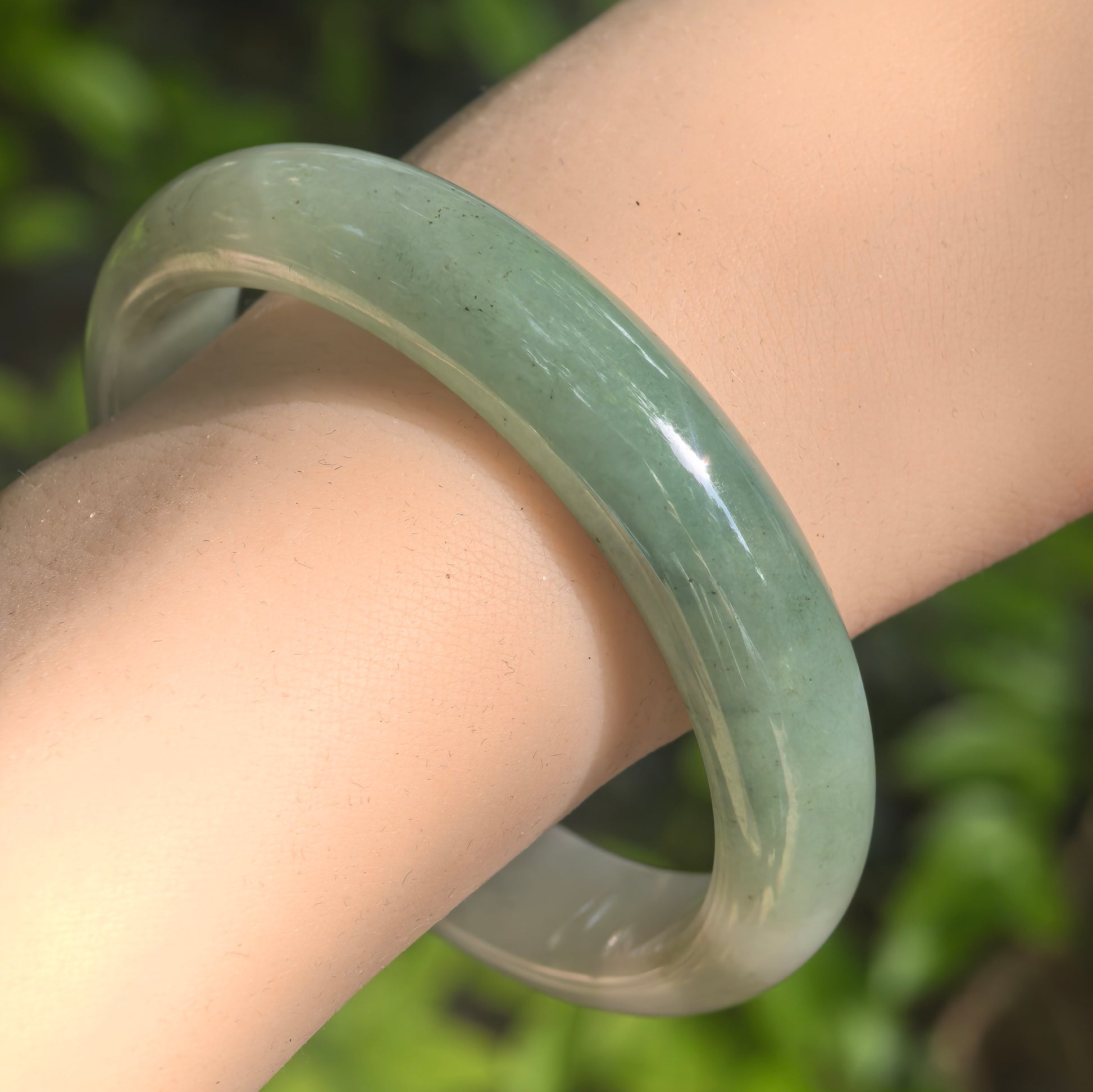 Natural Grade-A glutinous light green D-shape jadeite bangle worn on the wrist in natural light.
