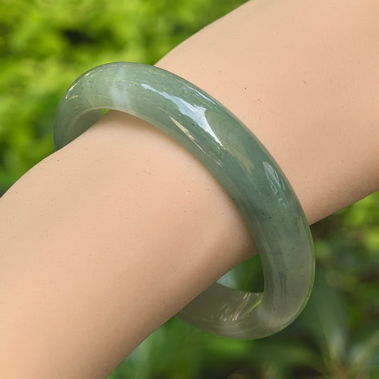 Close-up of glutinous light green jadeite bangle showing smooth polish and visible cotton patches.
