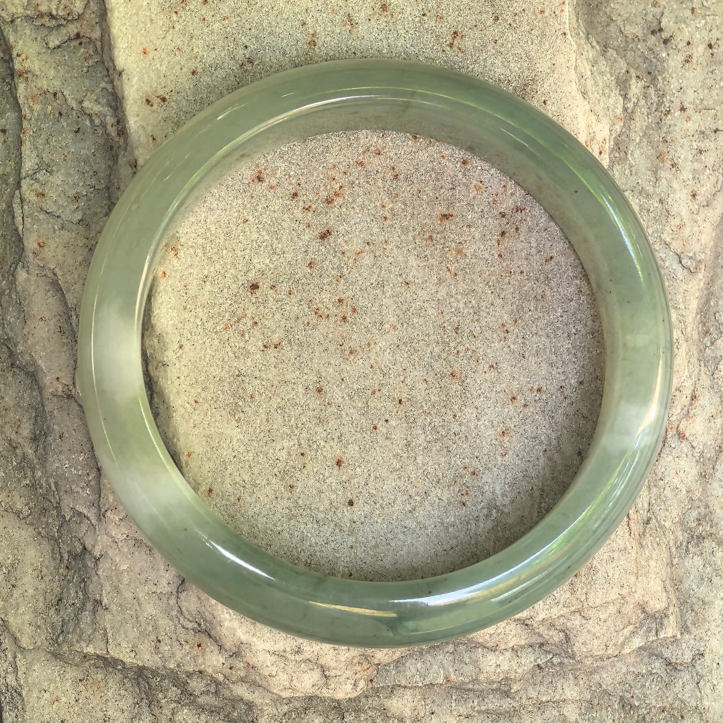 Natural Grade-A light green D-shape jadeite bangle displayed flat on a stone background.
