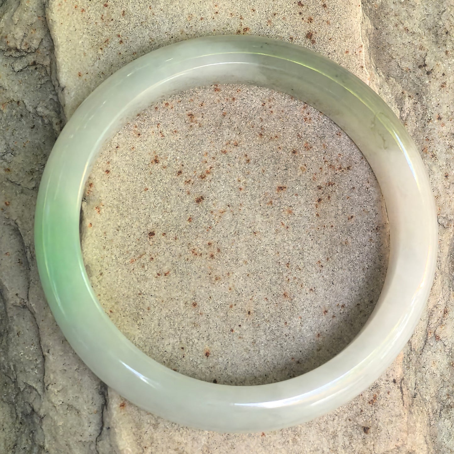 Natural Grade-A white-based green D-shape jadeite bangle displayed from above on stone background.
