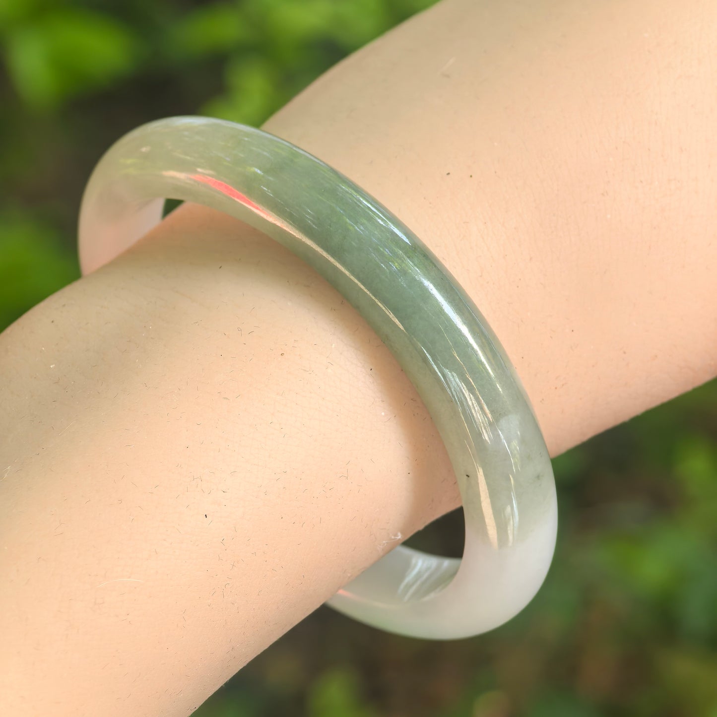 Natural Grade-A glutinous white-based dark green oval jadeite bangle worn on the wrist in natural light.
