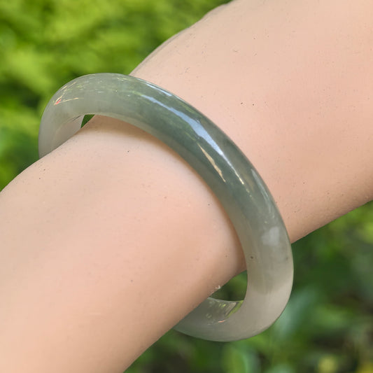 Close-up of glutinous white-based dark green jadeite oval bangle showing smooth polished surface.
