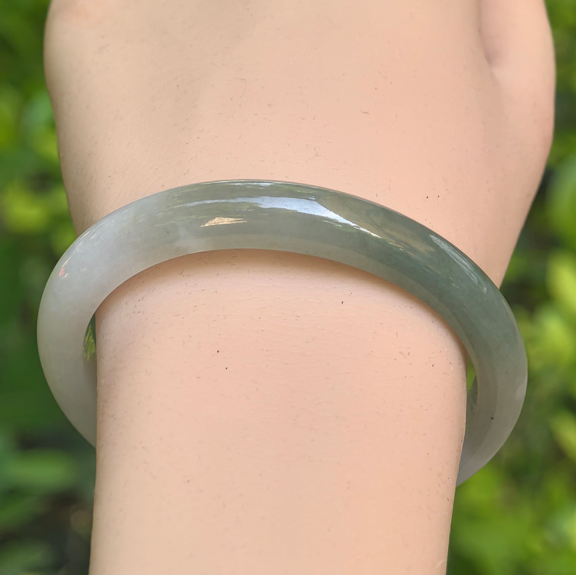 White-based dark green glutinous jadeite oval bangle shown from above with rounded polished shape.
