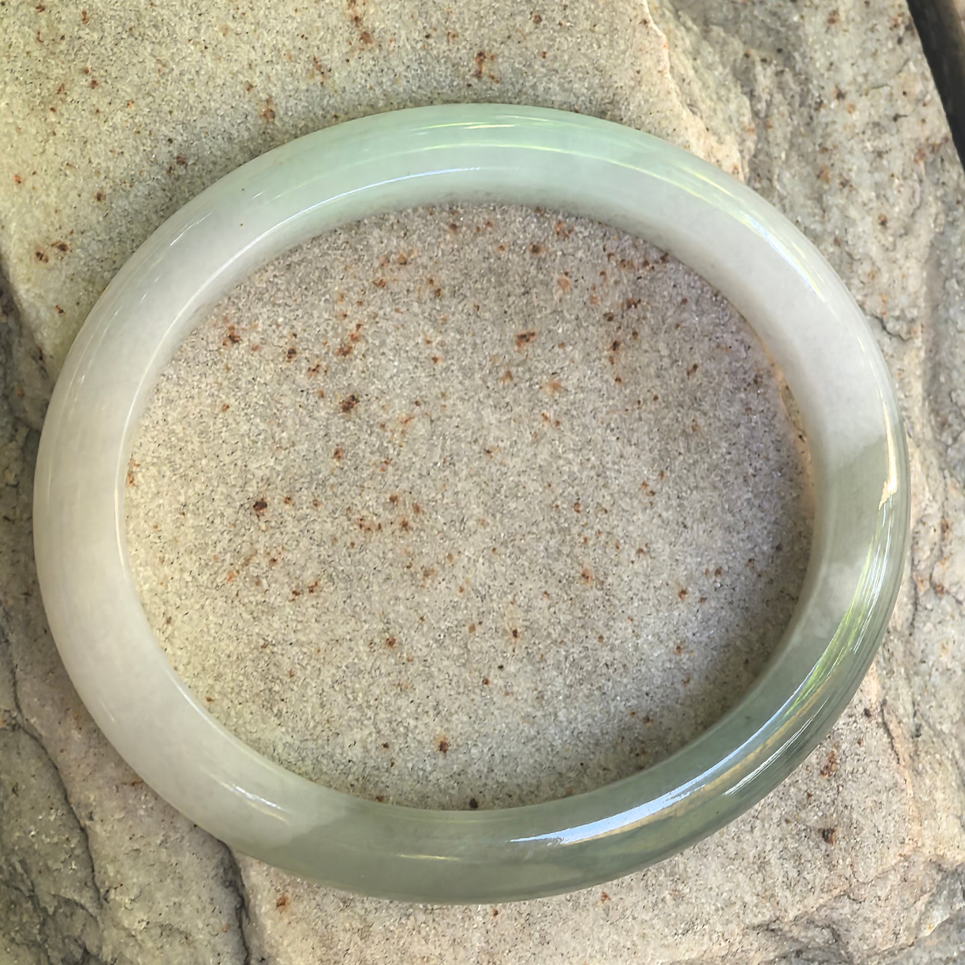 Natural Grade-A oval jadeite bangle with white base, dark green areas, and cottony inclusions displayed flat.
