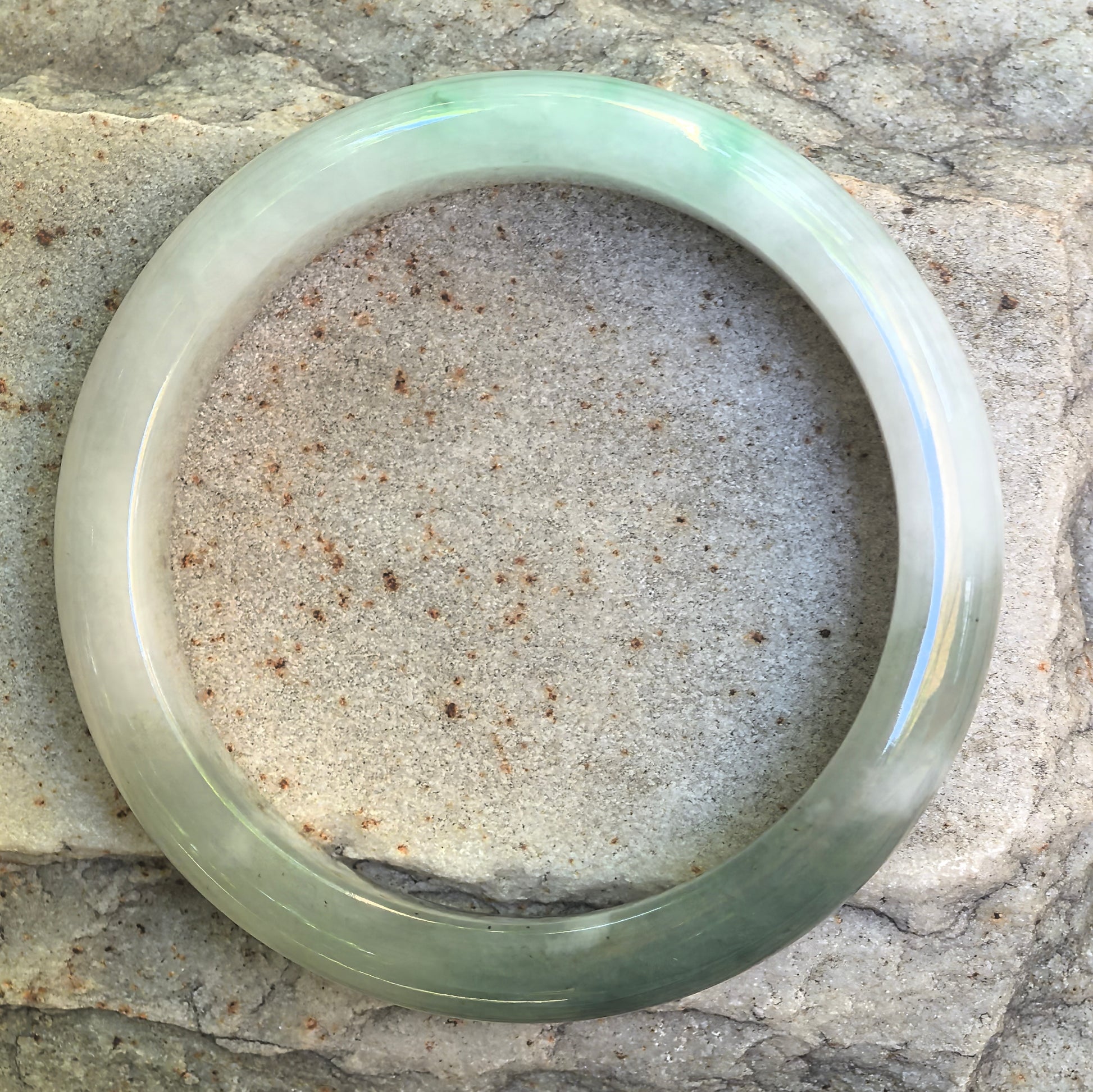 Close-up of white-based dark green jadeite bangle showing smooth polish and cottony inclusions.
