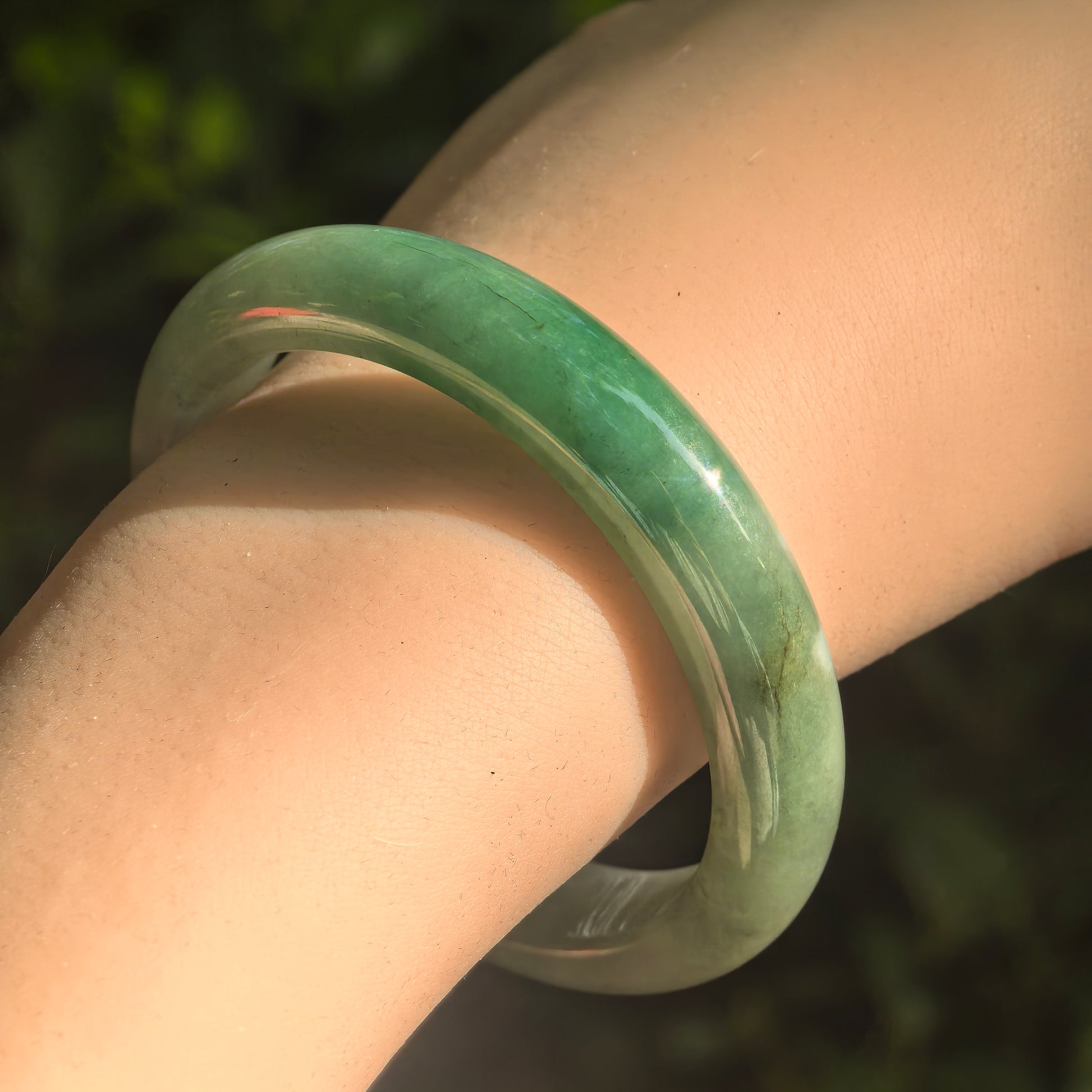 Natural Grade-A fine glutinous green D-shape jadeite bangle worn on wrist in natural light.
