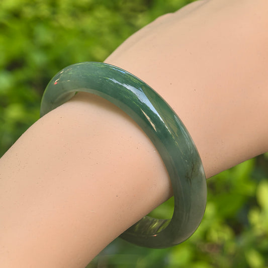 Close-up of green jadeite bangle showing glossy polish and visible surface-reaching crack.
