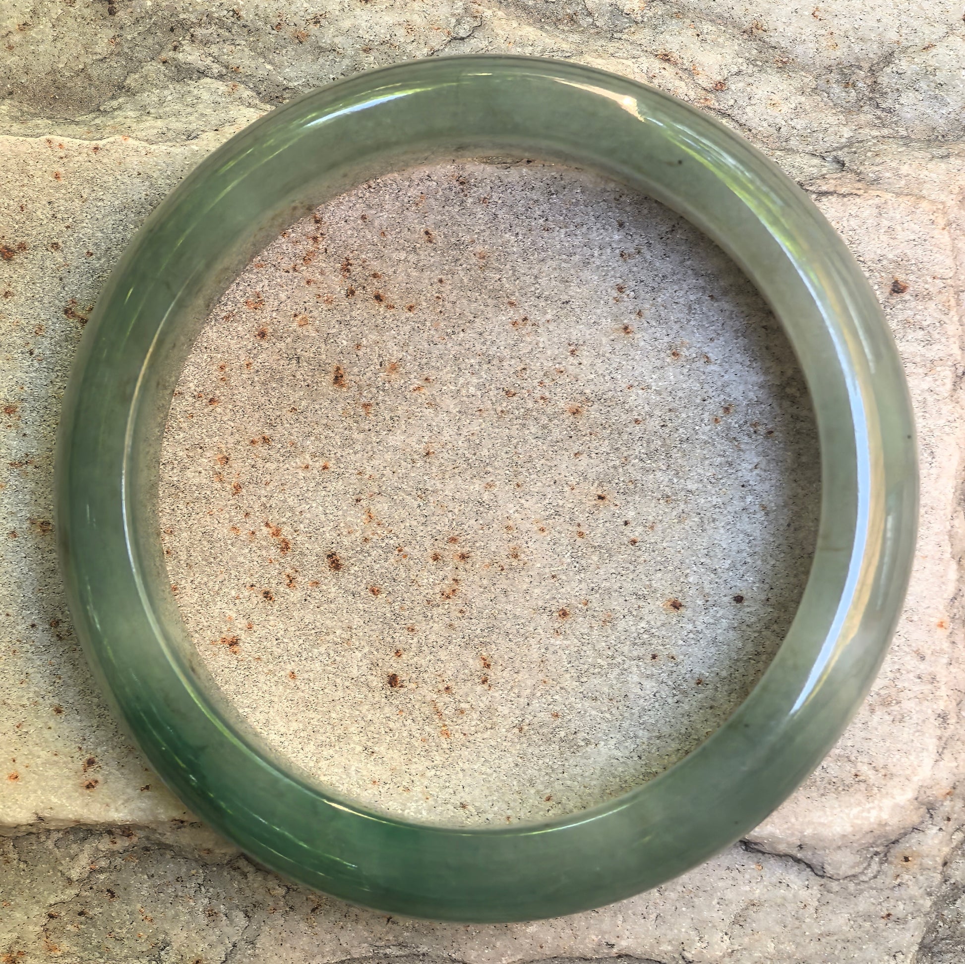 Natural Grade-A green D-shape jadeite bangle shown flat on stone background.

