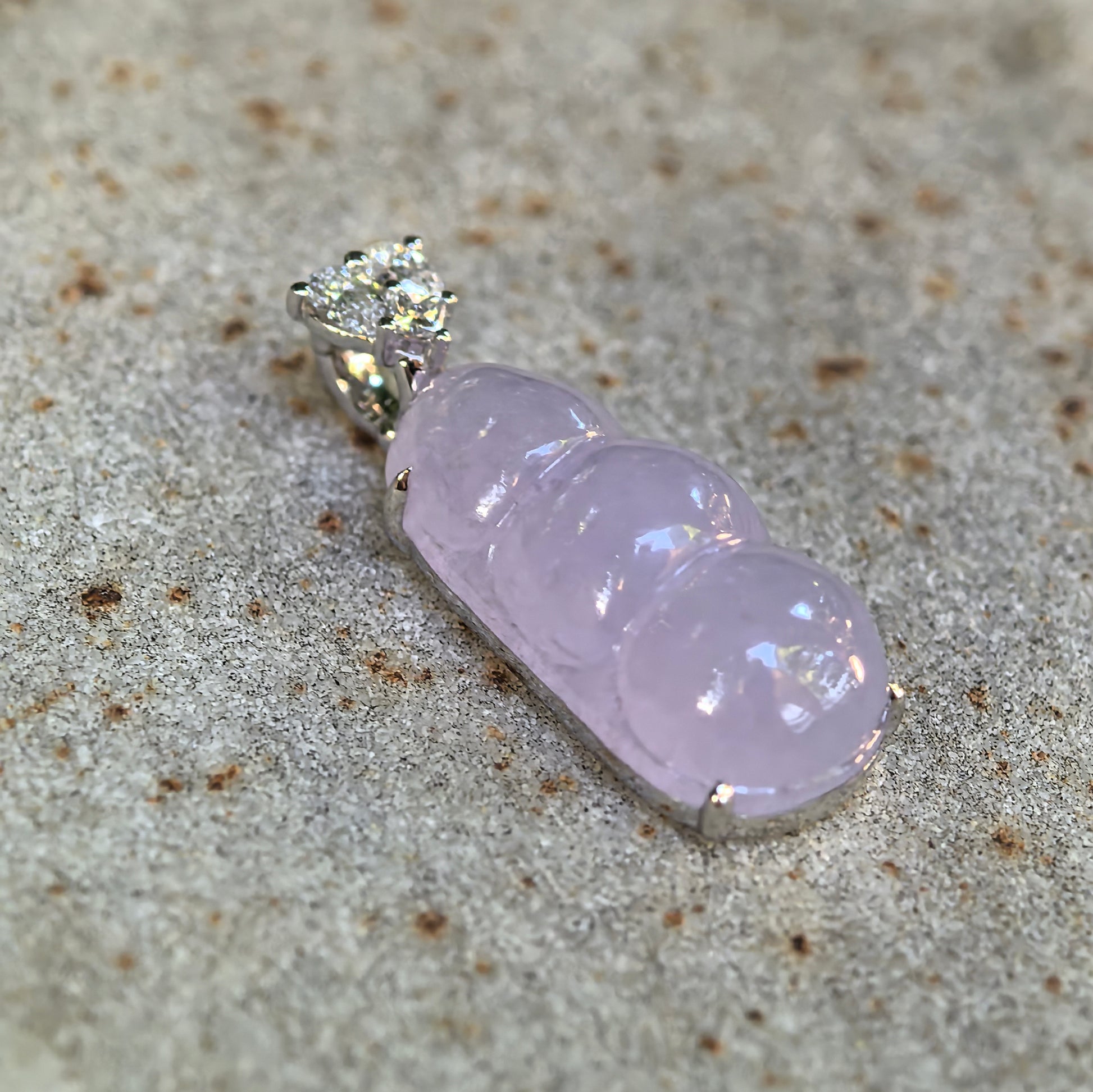 Side view of icy glutinous light lavender jadeite bean pod pendant on stone surface.
