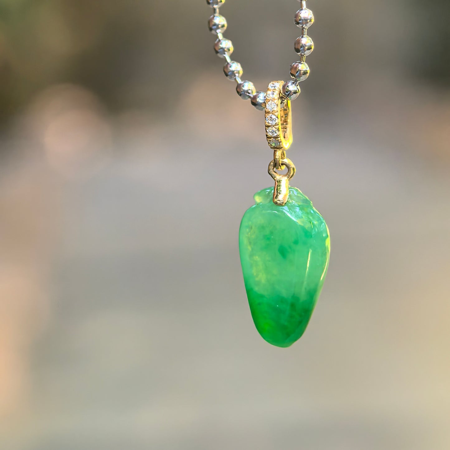 Close-up of vivid green bamboo leaf jadeite pendant with 18K gold diamond-accented bail.
